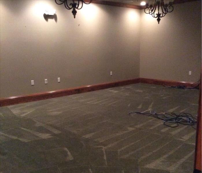 empty room with green carpet, wood baseboards, tan walls, and two iron chandeliers