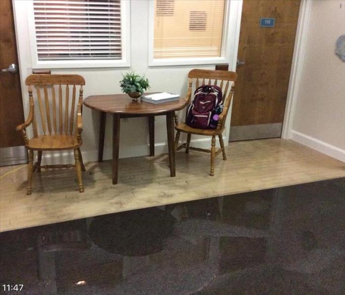 small wood table and two wooden chairs outside of room at senior living facility with water covering the floors