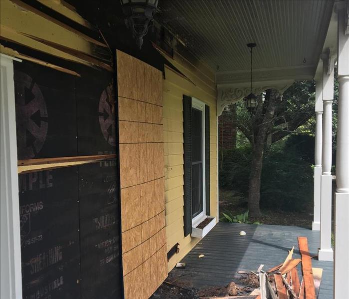 boarded up window on front porch of house with yellow siding