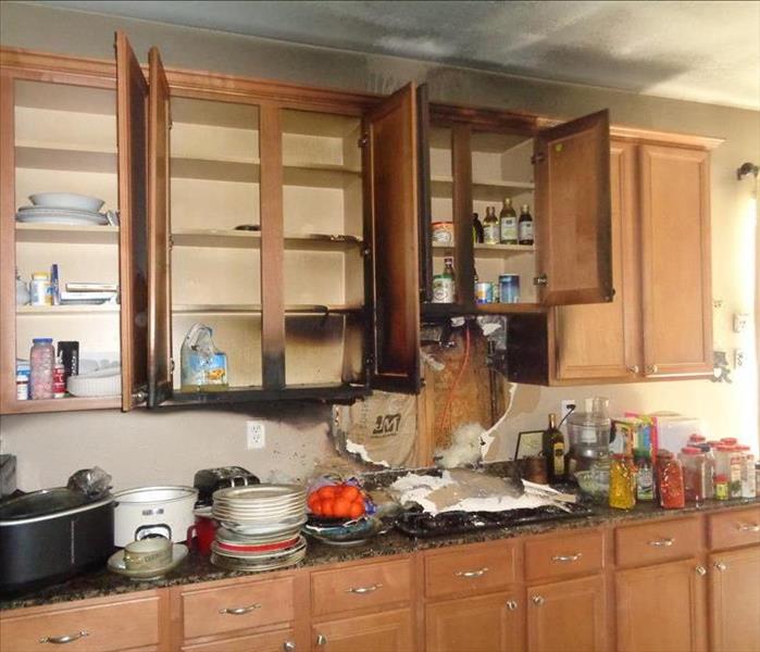 kitchen wall with top cabinets open and showing fire damage and bottom counter full of plates and food