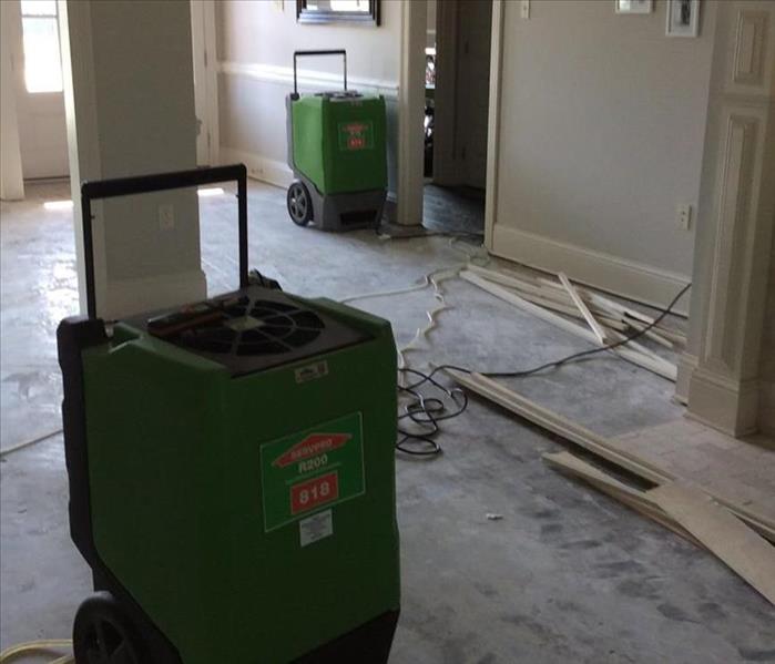 green dehumidifiers in living room with flooring removed and baseboard on ground