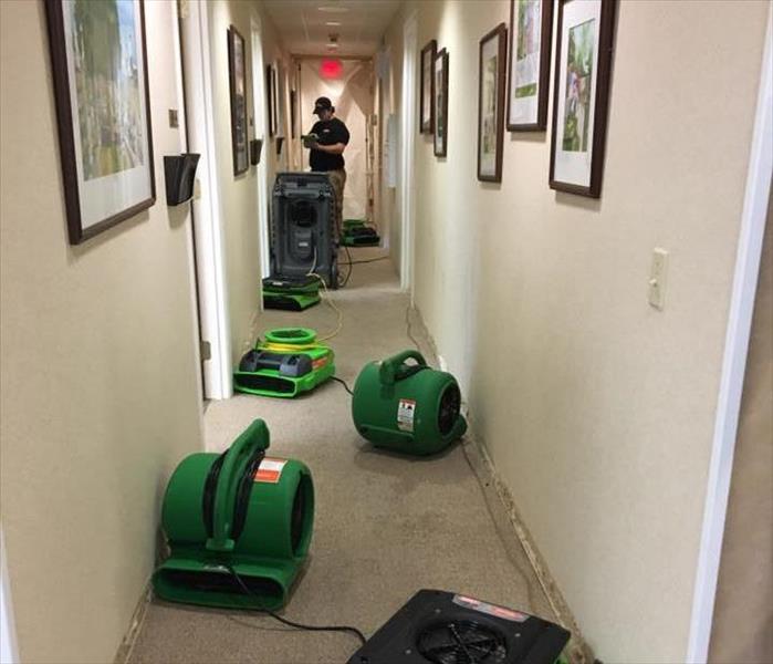 hallway with green fans and dehumidifiers with servpro technician at back end of hallway recording notes