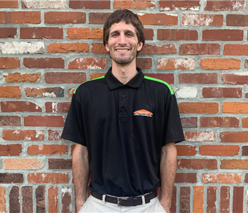 servpro water technician in black shirt and khaki pants standing in front of brick wall 