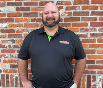 man in khakis and black SERVPRO shirt standing in front of brick wall