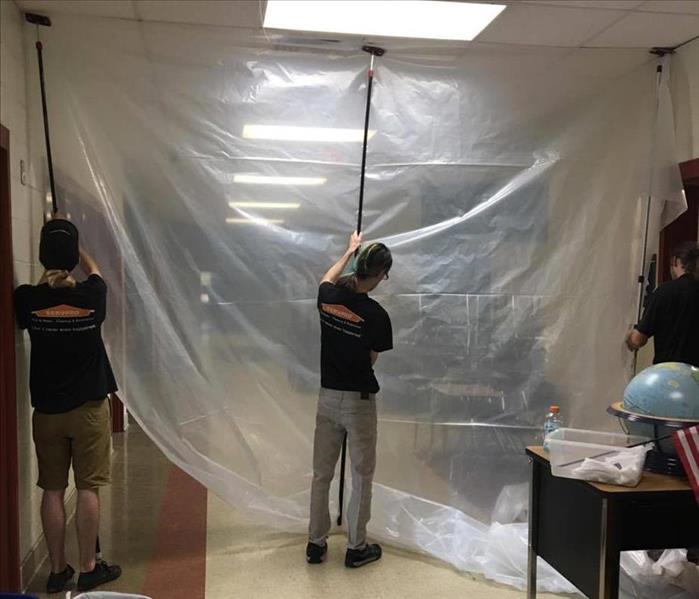 three men in black SERVPRO branded tshirts and khaki pants using poles to set up plastic containment in hallway