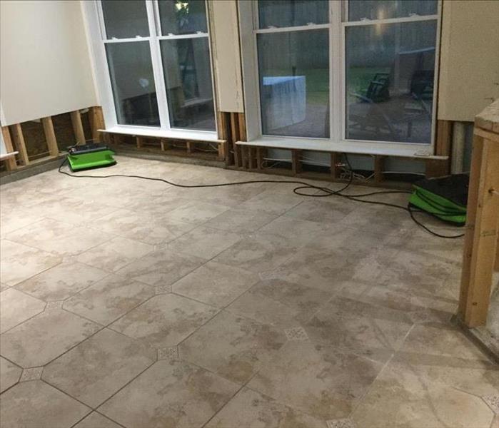 empty room with white tile, green fans drying exposed studs where sheetrock has been removed 