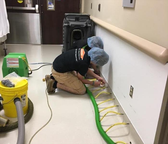 two employees in black shirts and khaki pants plugging drying tubes into wall in hallway