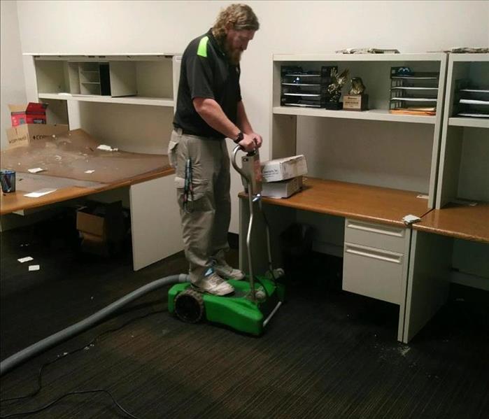 SERVPRO water restoration technician standing on water extraction equipment in office room