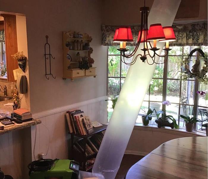 green fan with plastic cylinder taped to ceiling of living room with hole exposed