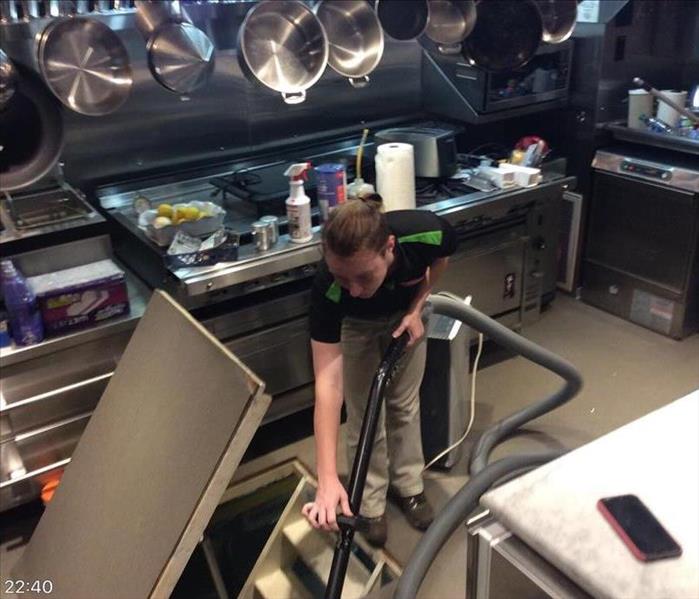 woman in black shirt and khaki pants extracting water in kitchen full of stainless steal appliances and hanging pots 