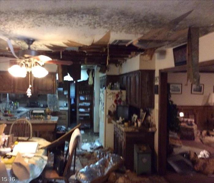 cluttered kitchen and dining room with hole in ceiling and black mold growing around it 