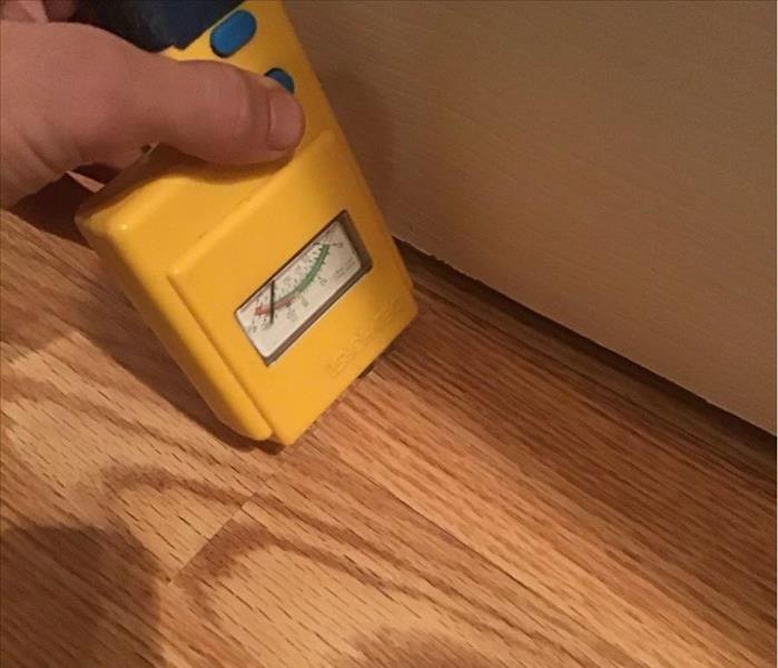 Moisture meter being held to the flooring to detect trapped water 