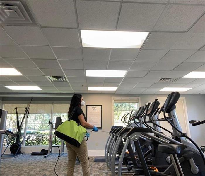 woman wearing mask spraying cleaner in gym 
