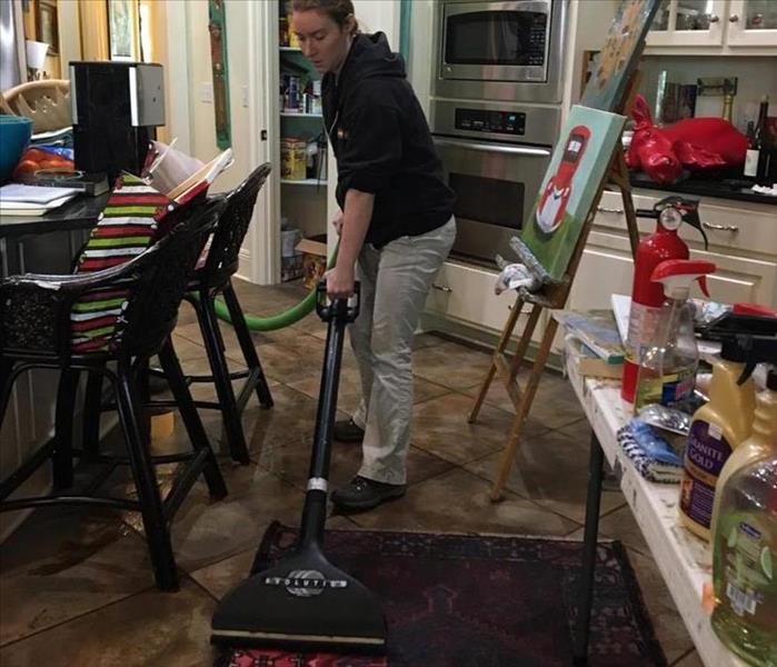 woman in black long sleeve shirt and khaki pants extracting water from a red rug in a kitchen