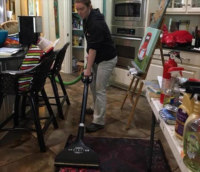 woman in black long sleeve shirt and khaki pants extracting water from a red rug in a kitchen