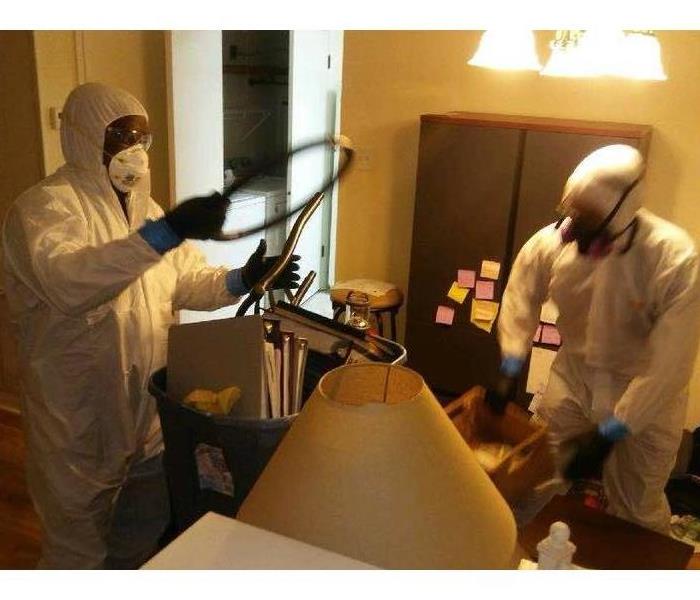 two technicians in personal protective equipment, gloves, respirators, and white hazmat suits, cleaning room