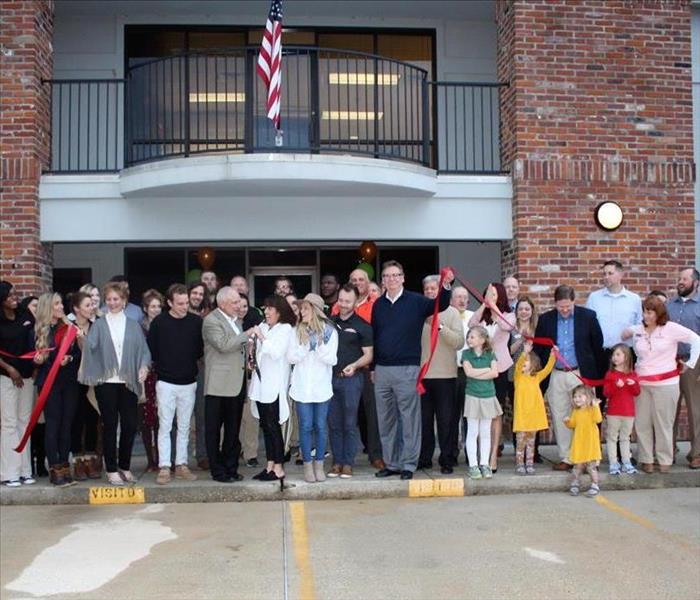 group of people standing in front of SERVPRO of Greater Covington and Mandeville cutting a red ribbon