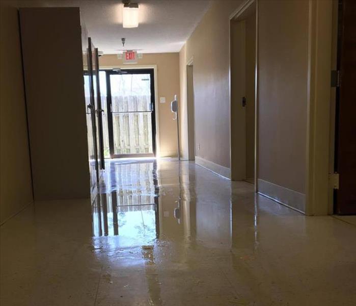 short hallway with glass door at end and water on tile floor 
