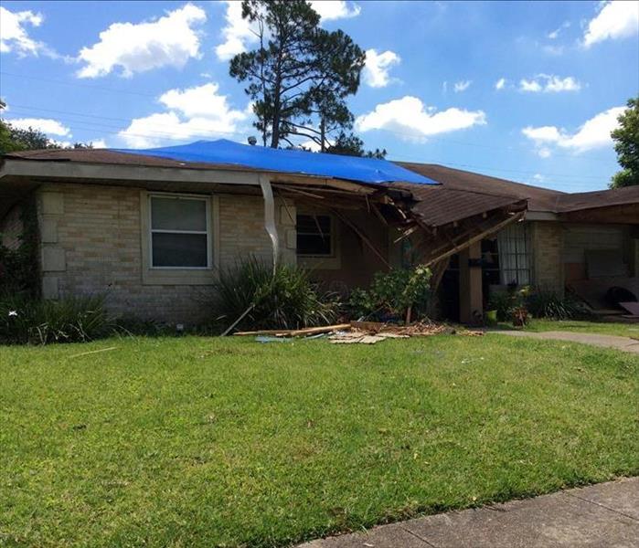 house with blue tarp on roof and part of roof crumbling into yard
