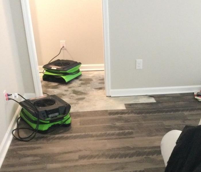 gray vinyl flooring half removed in room with two green air movers 