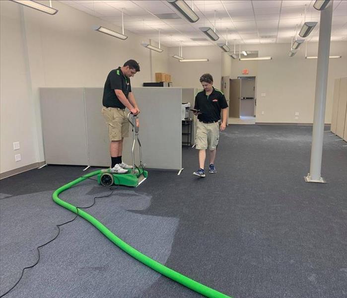 guy on standing water extractor extracting water from carpet in office space with other guy walking by