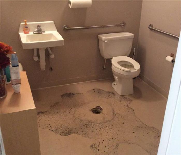 white toilet in commercial bathroom with black water stain on floor