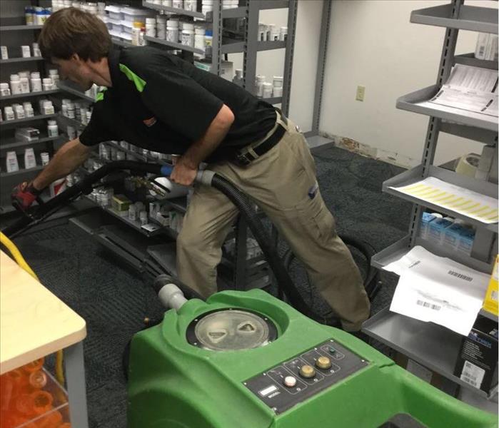 man in SERVPRO uniform is seen extracting water in a pharmacy stock room 